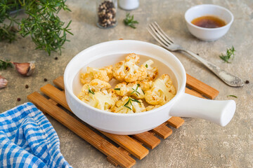 Baked cauliflower with melted brown butter in a portioned baking dish on a gray concrete background. Vegan recipes.