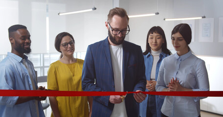 Portrait of smiling diverse young businesspeople cutting red ribbon in new office
