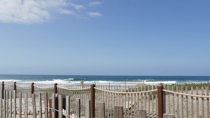 Pacific ocean coast, greenery and wooden picket fence on sea shore. Blue water waves on sunny summer beach, Encinitas shoreline, California USA. Coastline near Los Angeles. Coastal access entrance.