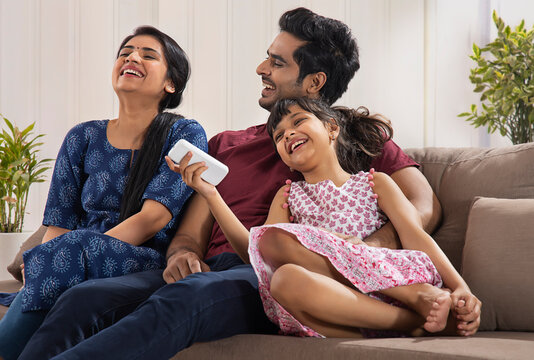 A CHEERFUL FAMILY HAPPILY LAUGHING TOGETHER WHILE SITTING COMFORTABLY AT HOME	