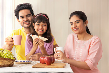  A CHEERFUL FAMILY LOOKING AT CAMERA WHILE EATING BREAKFAST	