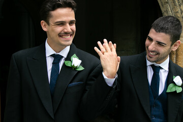Gay couple laughing and smiling and they leave church after getting married, pointing at each...