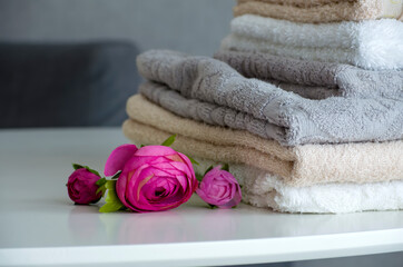 A stack of terry shower towels on a white table close-up next to artificial peony flowers