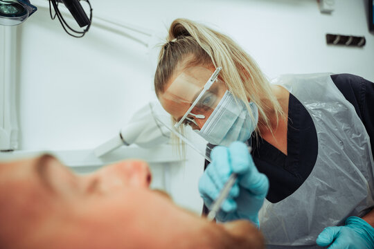 Caucasian male client sitting in dentist chair while nurse evaluates dirty teeth