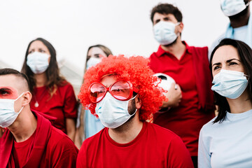 Group of football team supporters in red and blue t-shirt and protective face mask watching...