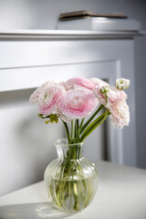 the Bouquet of pale pink Persian buttercups on the table against the background of the fireplace.