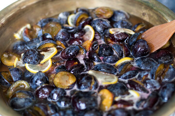 Cooking plum jam with lemon and spices in a copper basin on a gas stove.
