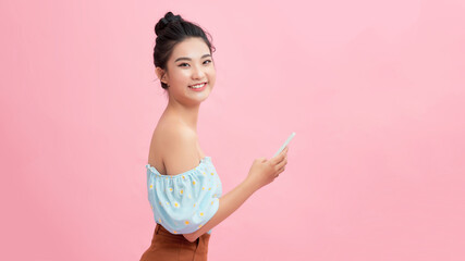 Portrait of a smiling casual woman holding smartphone over pink background