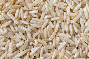 A macro background texture portrait of a pile of uncooked raw hard whole rice grains. The food is ready to be boiled and cooked as a side dish to a delicious meal.