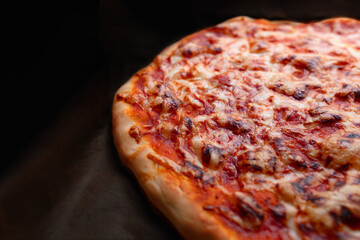 Homemade freshly baked pizza with cheese and golden crust on dark background