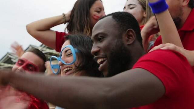 Multiracial group of spectators in team colours watching sports event at stadium