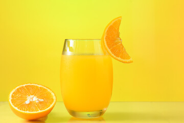 one glasses with orange juice, half an orange next to the glass on the yellow background