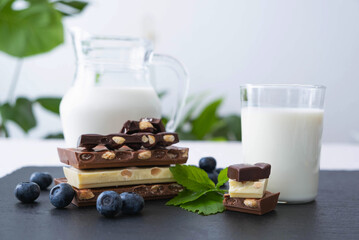 broken bars of black, white and milk chocolate with blueberry berries nuts and a jug of milk