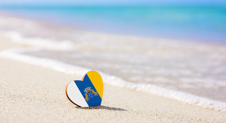 Flag of the Canary Islands in the shape of a heart on a sandy beach. The concept of the best vacation in Canary Islands