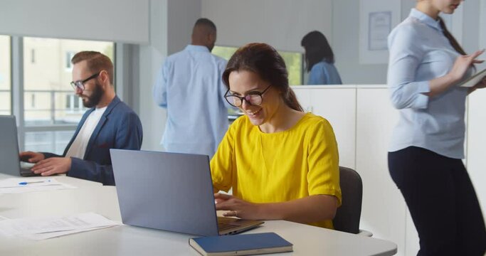 Happy young businesswoman using computer at workplace in modern office