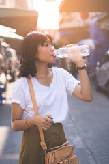 Portrait of Asian young woman  drinking water from a bottle at street market in bangkok, Thailand.