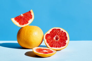 Fresh healthy grapefruit on sunlight with hard shadows. Minimal food creative concept on blue pastel background. Grapefruit slices citrus fruits.