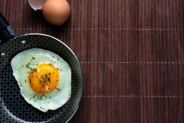 Frying pan with fried egg on a bamboo table
