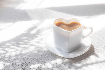 Obraz na płótnie Canvas A cup of cappuccino on a saucer and shade from the sun. Coffee drink. Copy space. A heart-shaped cup.