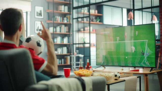 At Home Soccer Fans Sitting on a Couch Watch Football Game on TV, Cheer for Favourtite Sports Team to Win Championship. Screen Shows Professional Football Club Play. Over the Shoulder