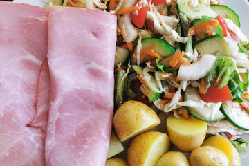 Ham salad with boiled baby potatoes and vegetables included cucumber, tomatoes, onion, cabbage, lettuce and carrot on a plate.  Healthy and dietary food. 