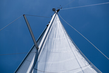 Yacht sails on clear blue sky background. Sailing with the wind at open sea ocean, summer holidays