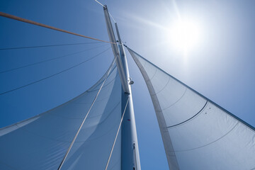 Yacht sails on clear blue sky background. Sailing with the wind at open sea ocean, summer holidays