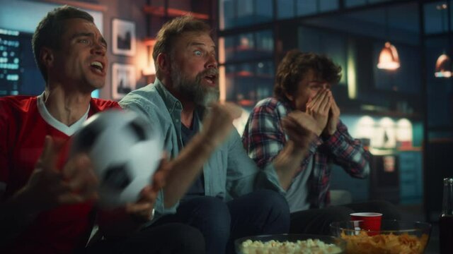 Night At Home: Three Joyful Soccer Fans Sitting on a Couch Watch Game on TV, Celebrate Victory when Sports Team Wins Championship. Group of Friends Cheer When Favourite Football Club Play.