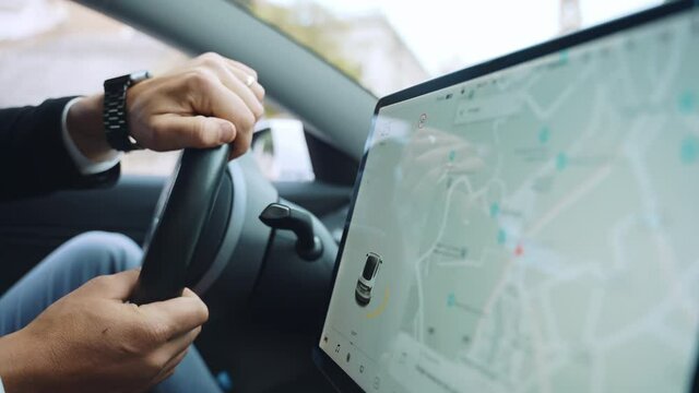 Side view of person's hands holding steering wheel while driving a car on the street road, businessman using touch screen monitor for navigation apps and other online functions. Driver's hands on car