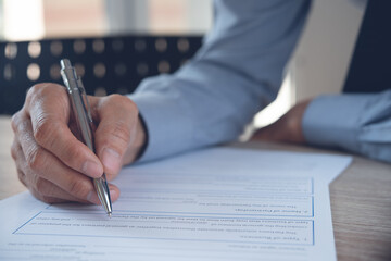 Business man hand with a pen signing contract, paper document on table in office, close up