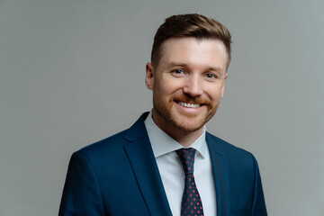 Happy successful entrepreneur in suit smiling at camera while posing against grey background