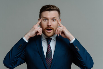 Amazed businessman in suit holding fingers on temples and looking at camera with shocked face expression