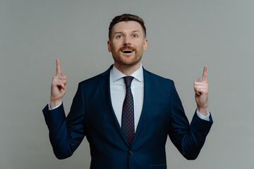 Shocked businessman in suit pointing up with fingers and looking with amazed face expression