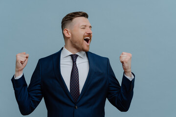 Excited businessman in suit keeping arms raised and screaming while celebrating success