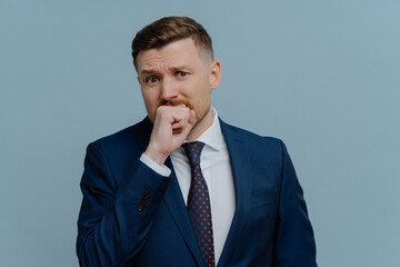 Nervous businessman biting fist emotionally and looking at camera