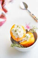 Peaches served in white plate with mascarpone, pink flower and herbs on the white background. Summer dessert.