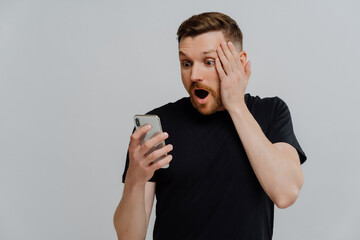 Impressed man reading stunning news on smartphone with shocked expression
