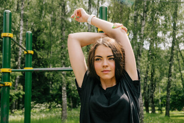 Russian girl in black performs a sports exercise on stretching hands on the playground
