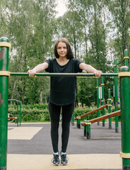 Fototapeta premium a girl in a black T-shirt and leggings shakes her hands from the horizontal bar on the playground