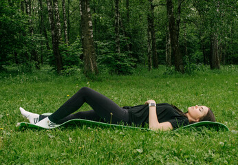 a girl in a black T-shirt and leggings lies on a sports mat and rests after classes in the green