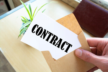Male hands holding craft envelope with word CONTRACT on blue background, communication concept
