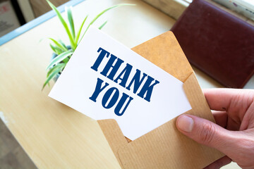 Male hand holding craft envelope with text THANK YOU on blue background