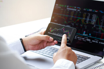 Close-up businessman hand holding phone and analysis finance market graph stock market trading,stock chart and investment concept.