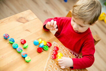 Counting game. Collect correct amount of caps by assigned number. Little boy perform the task....