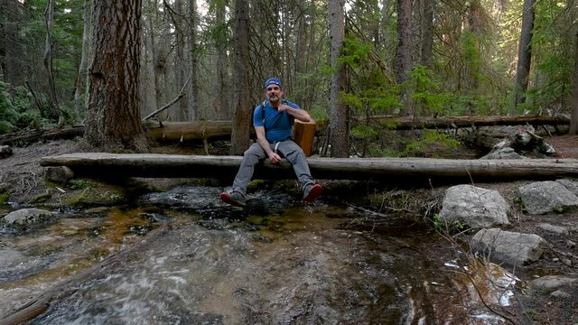 Hiker sitting on a log bridge by creek