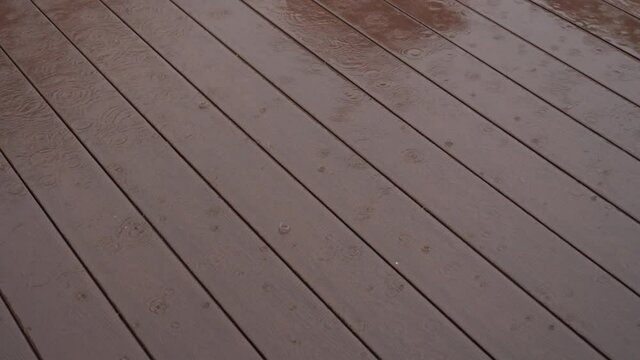 A brown composite outdoor floor with wood pattern. Heavy rain and large raindrops fall to the floor. A maintenance-free floor.