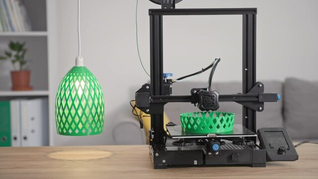 modern technologies, automatic 3D printer prints from molten green plastic a prototype of a lamp shade for a lamp at home