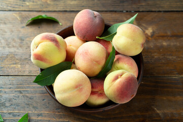 Ripe peaches with leaves in a clay bowl on a wooden table.