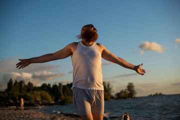 A humorous portrait of a brutal man in a T-shirt and boxers on the beach at sunset