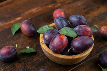 Fresh plums with leaves in a wooden bowl on a brown table.